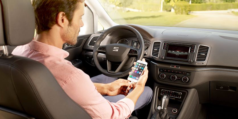 Hombre sentado en el interior de un SEAT Alhambra revisa hojas de rescate en su smartphone.