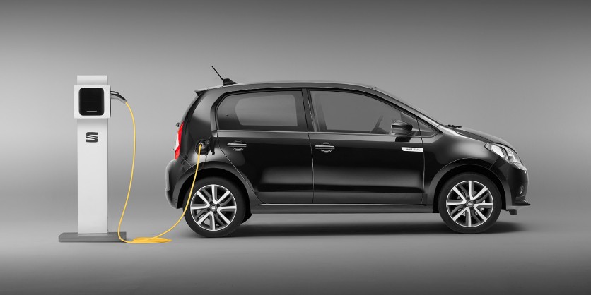Vista lateral de un SEAT Mii Electric conectado a poste de carga pública.