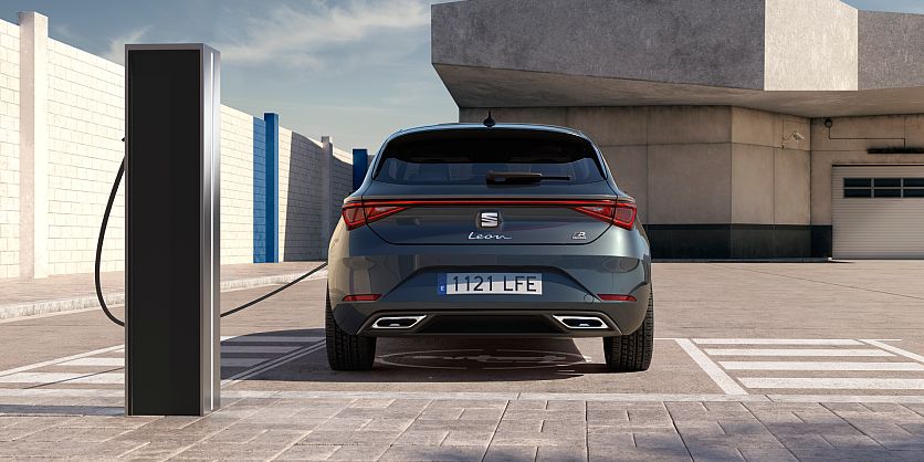Vista trasera de un SEAT León Sporstourer en gris magnetic conectado a estación de carga en aparcamiento público