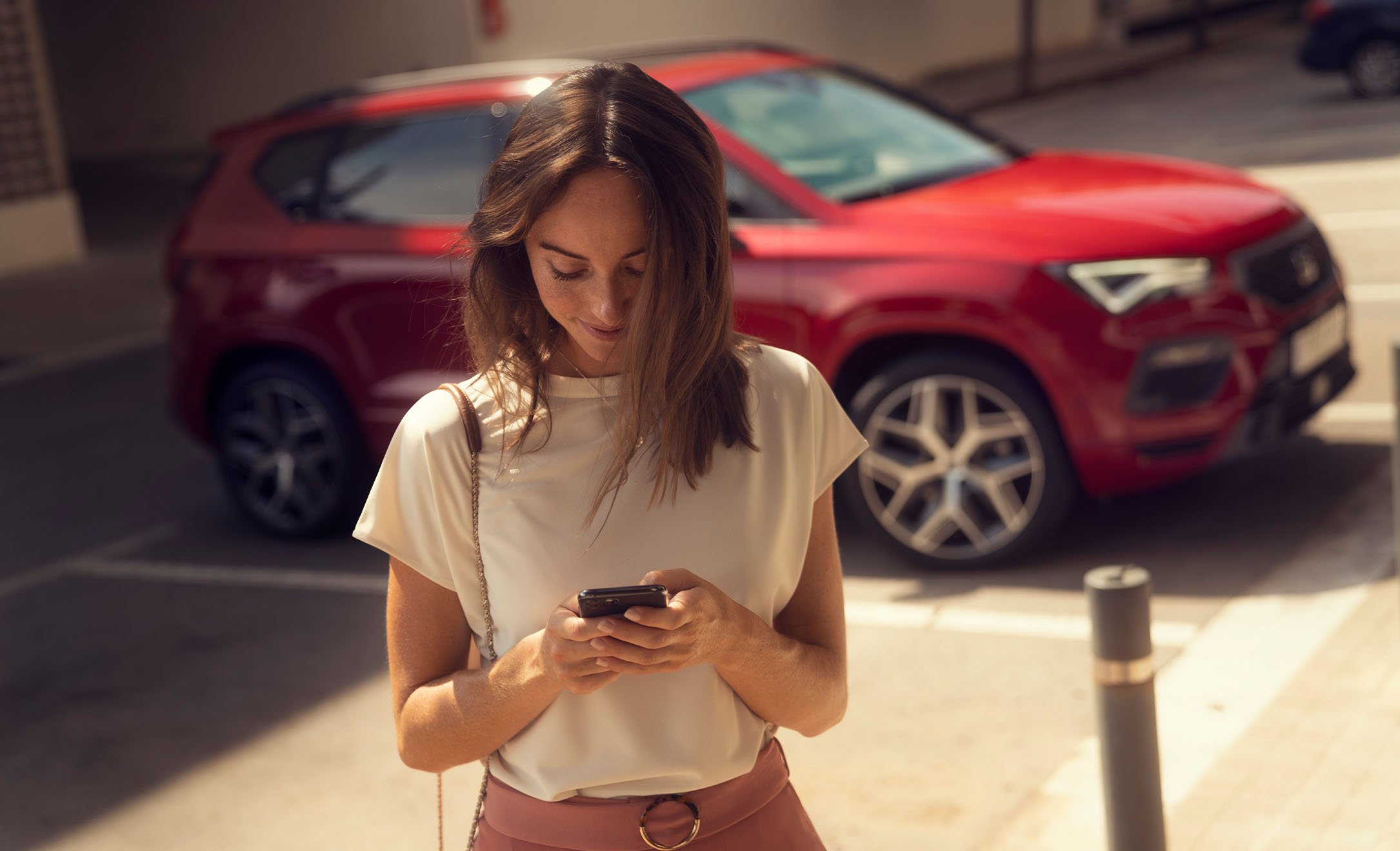 Mujer se aleja de SEAT Ateca FR rojo desire mirando pantalla de smartphone
