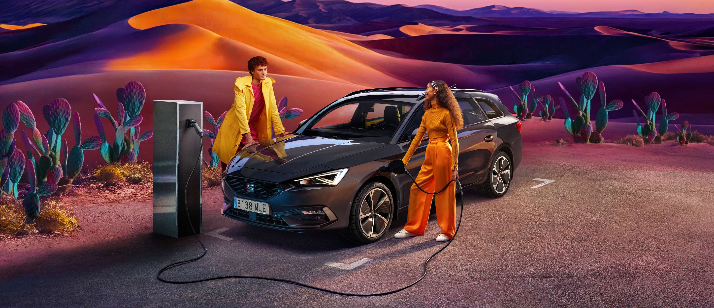 Hombre y mujer recargando SEAT Leó híbrido eléctrico enchufable en escenario con dunas