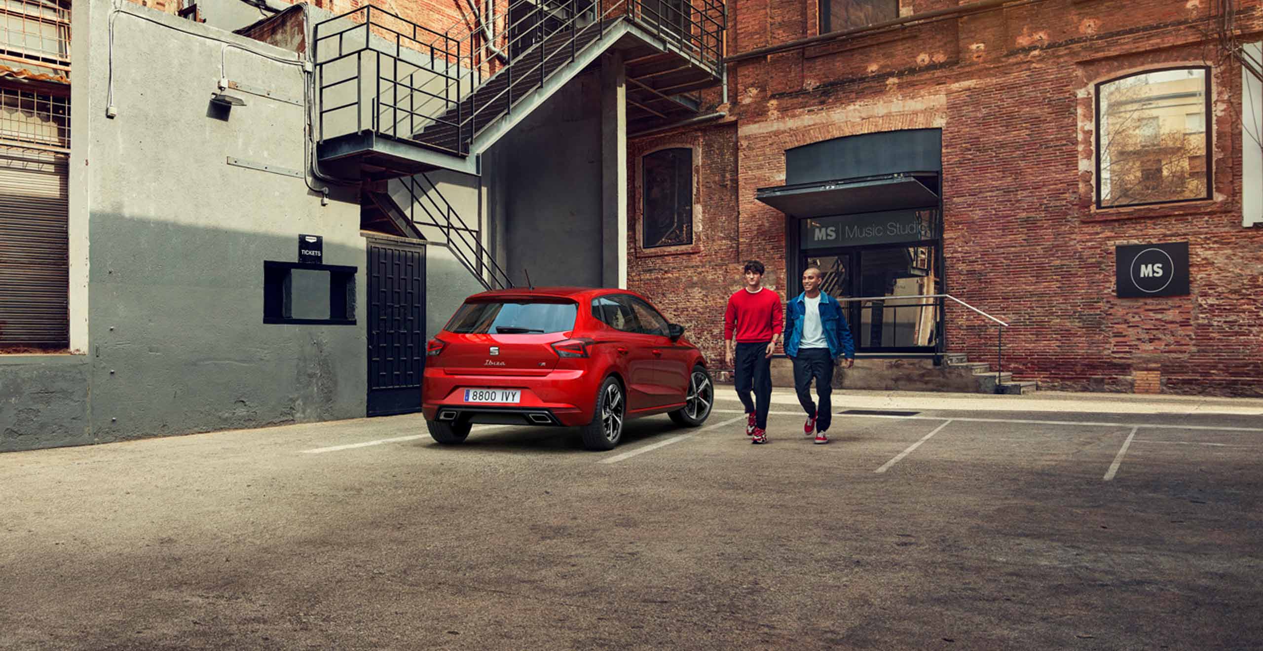 Hombre y mujer vistiendo la colección de SEAT al lado de su SEAT Ibiza