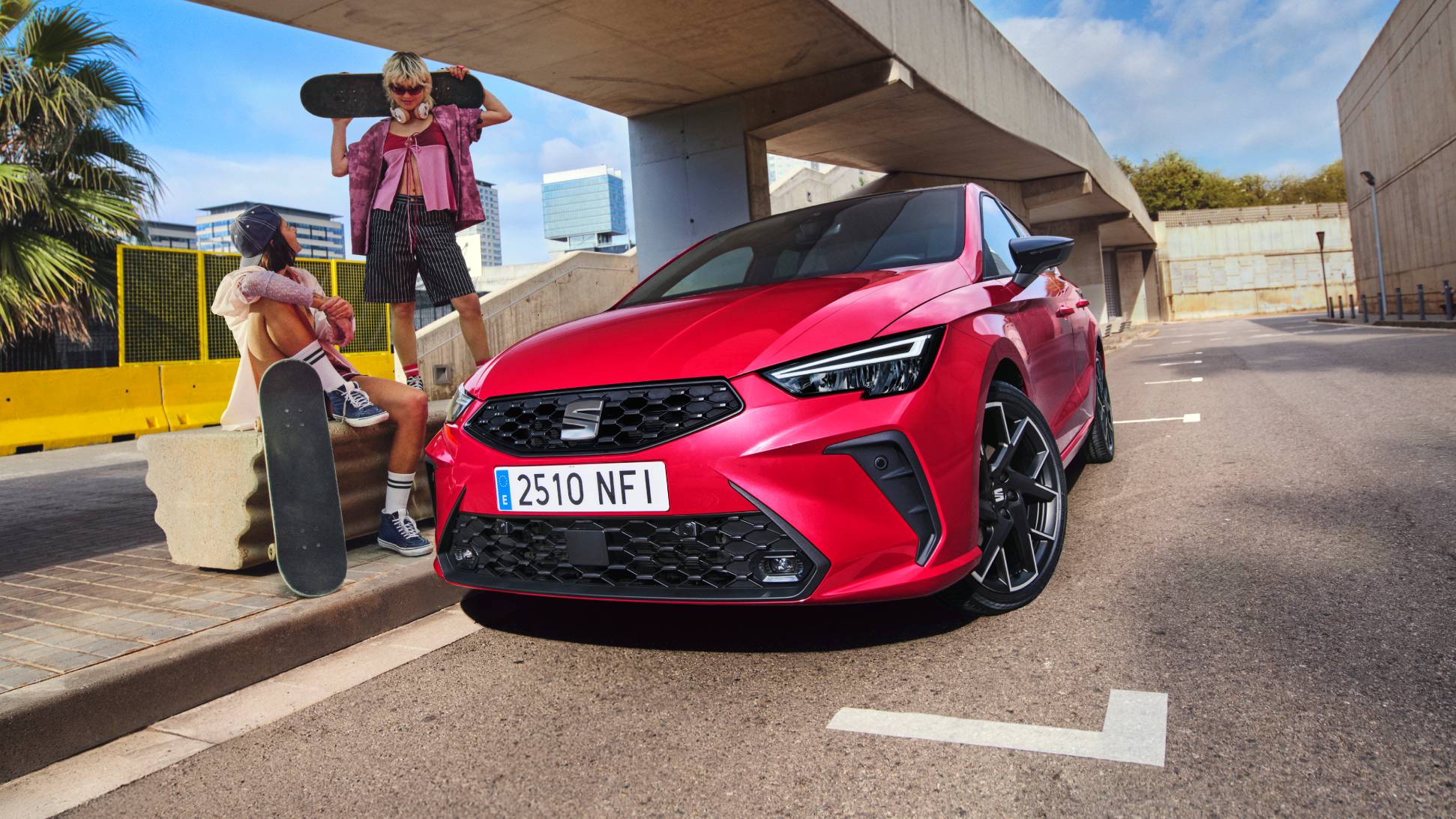 SEAT Ibiza en color rojo Liminal aparcado en entorno urbano bajo un moderno puente con dos personas y un skateboard