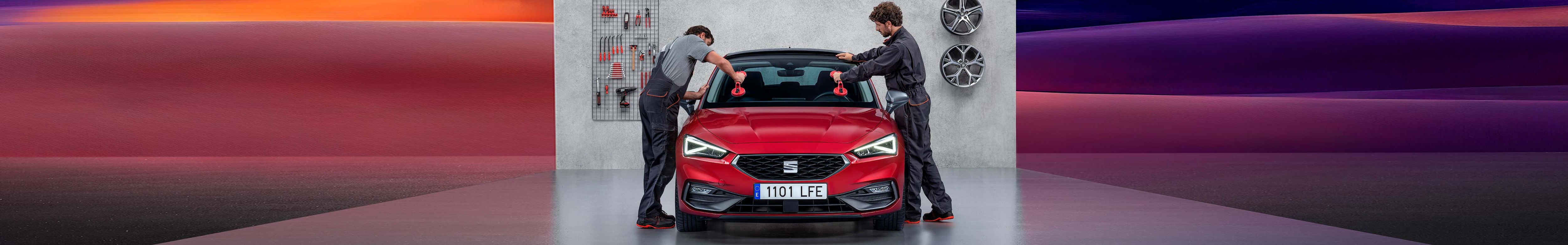        Especialistas realizan un cambio de parabrisas a un León rojo en taller de servicio posventa de SEAT