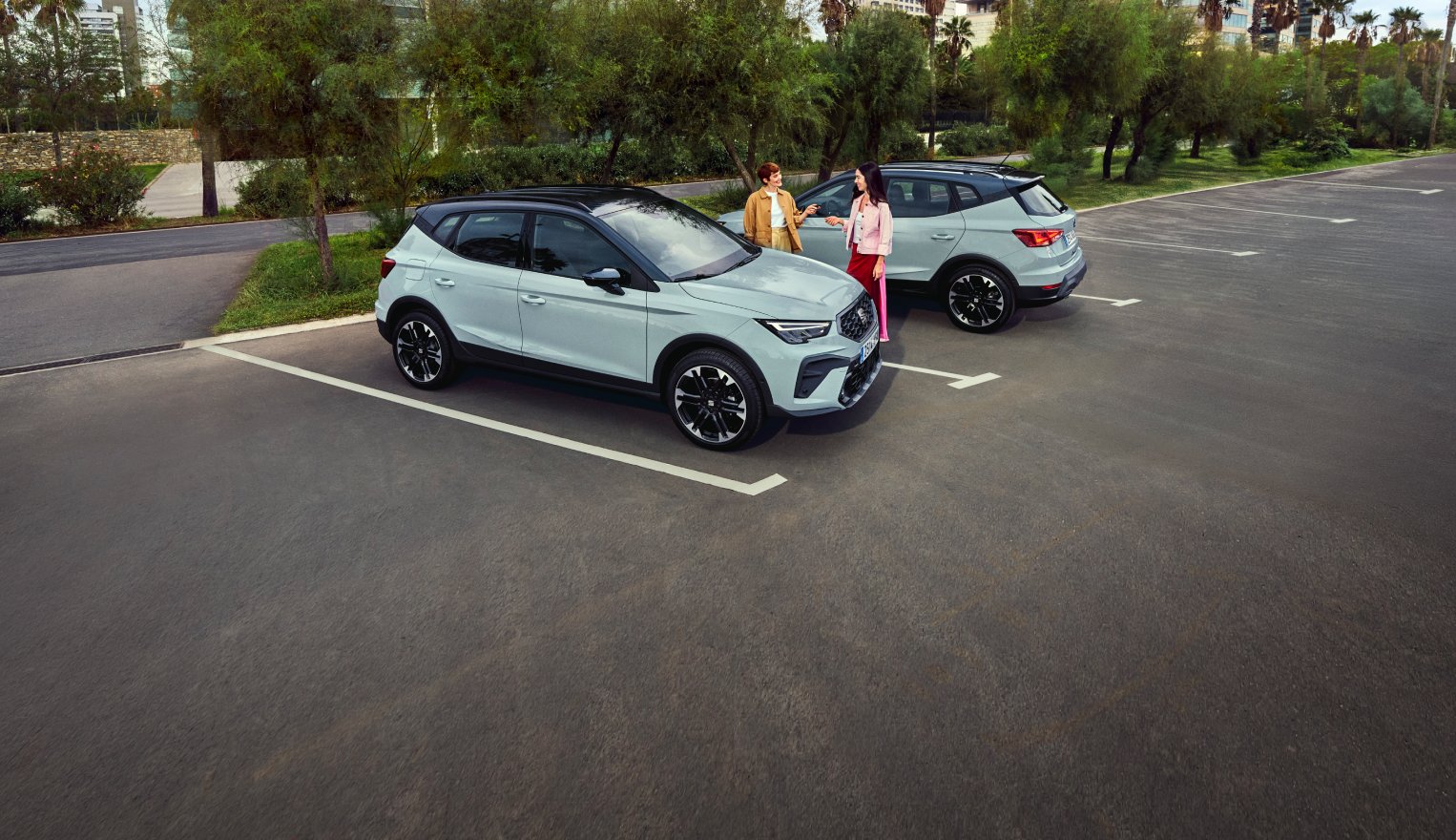 Dos mujeres conversando junto a dos SUVs compactos SEAT Arona Style 2026 de color oniric lake
