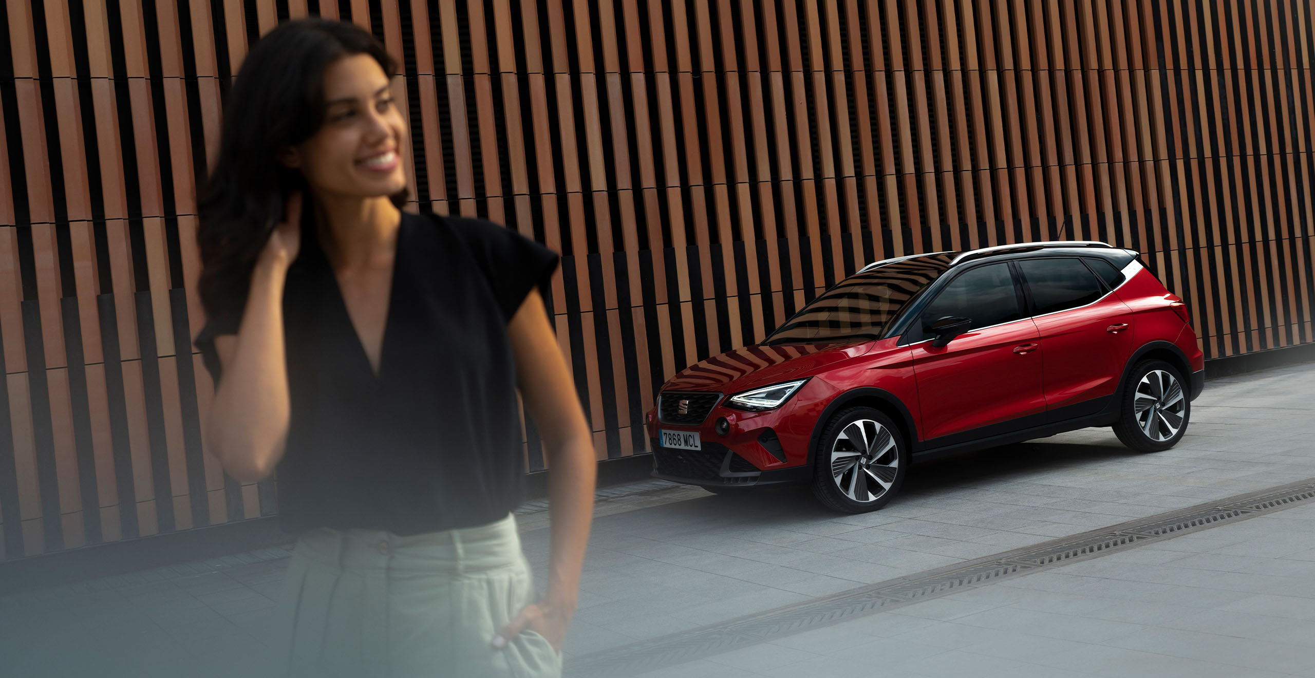 Mujer sonriendo mientras camina con SEAT Arona FR rojo desire al fondo