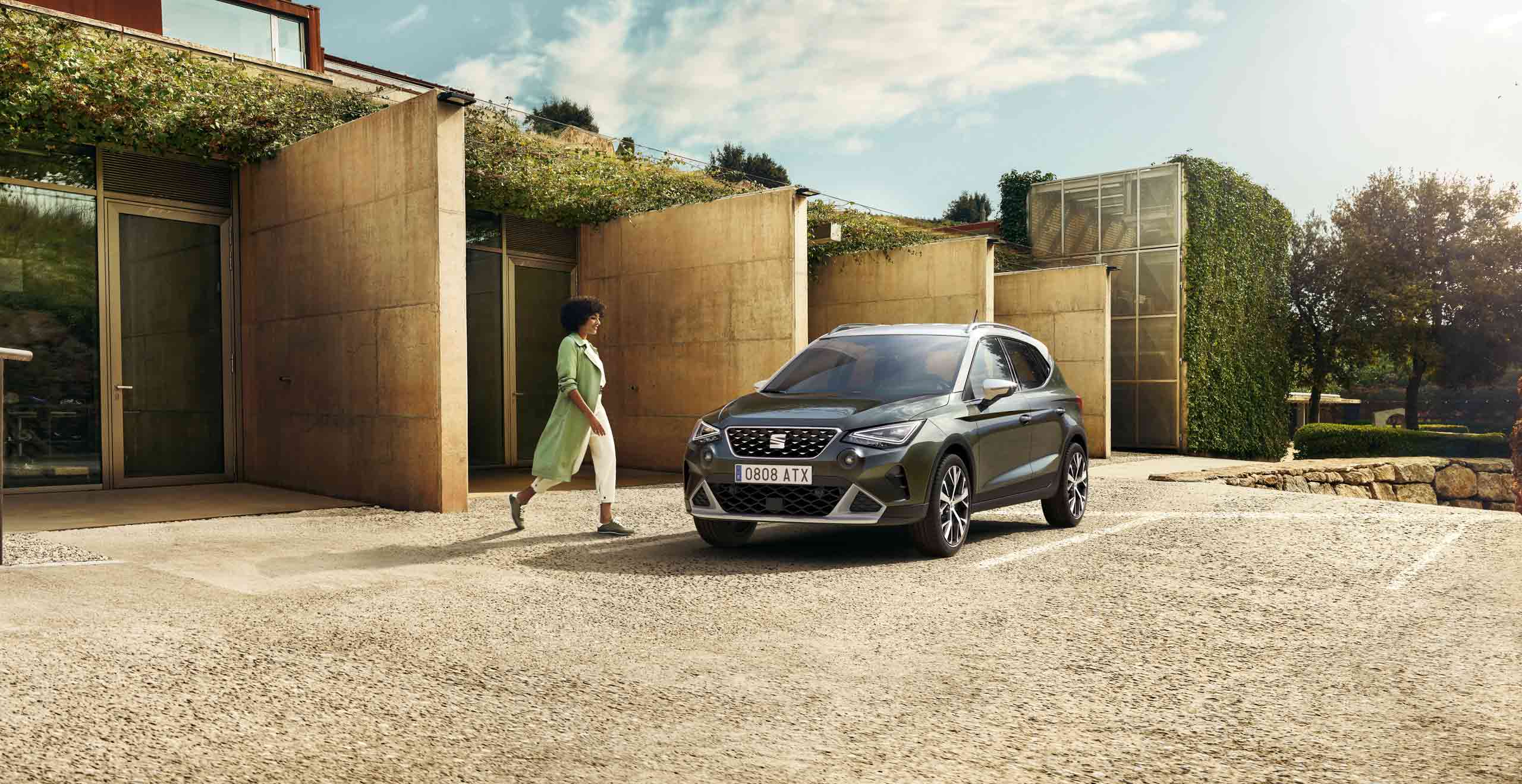 Mujer andando hacia el SEAT Arona color Dark Camouflage con techo blanco