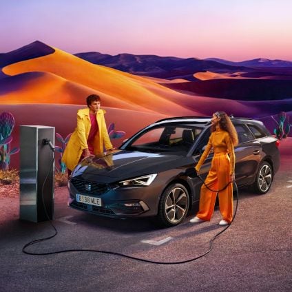 Hombre y mujer recargando SEAT Leó híbrido eléctrico enchufable en escenario con dunas