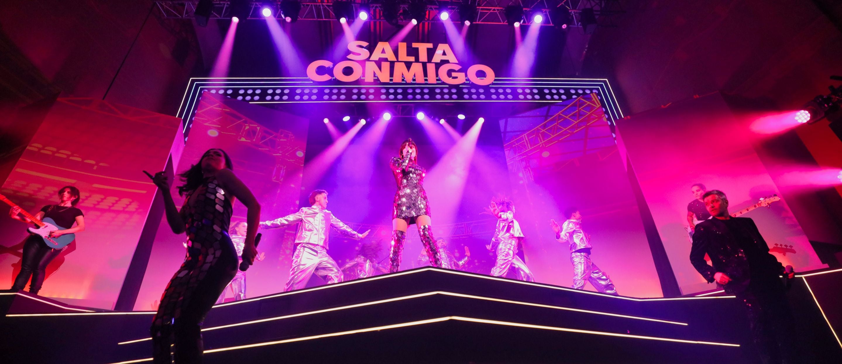 Escenario con artistas e iluminación morada interpretando canciones del musical Salta Conmigo de SEAT.