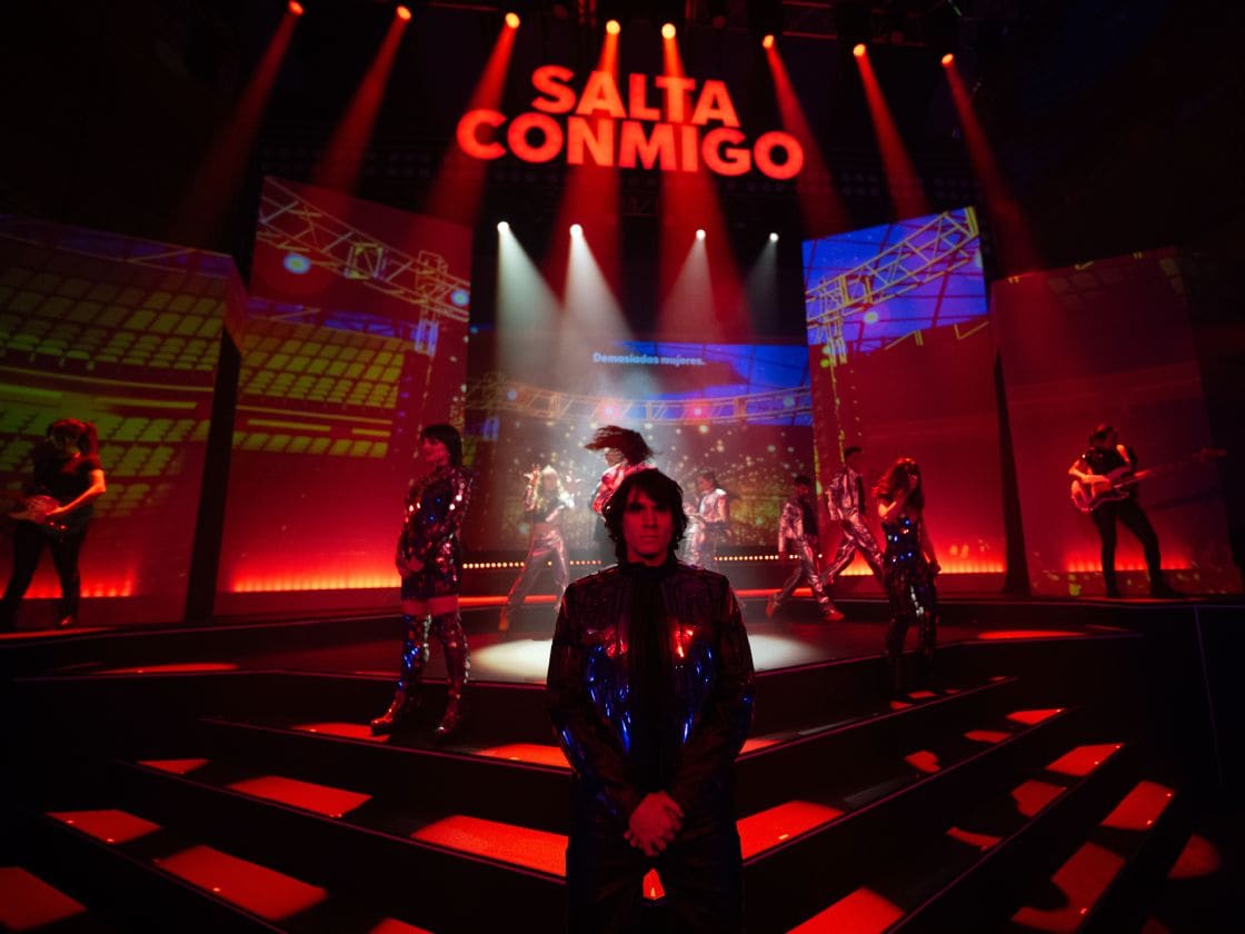 Artistas posan en escenario con iluminación roja antes de empezar uno de los temas musicales de Salta Conmigo