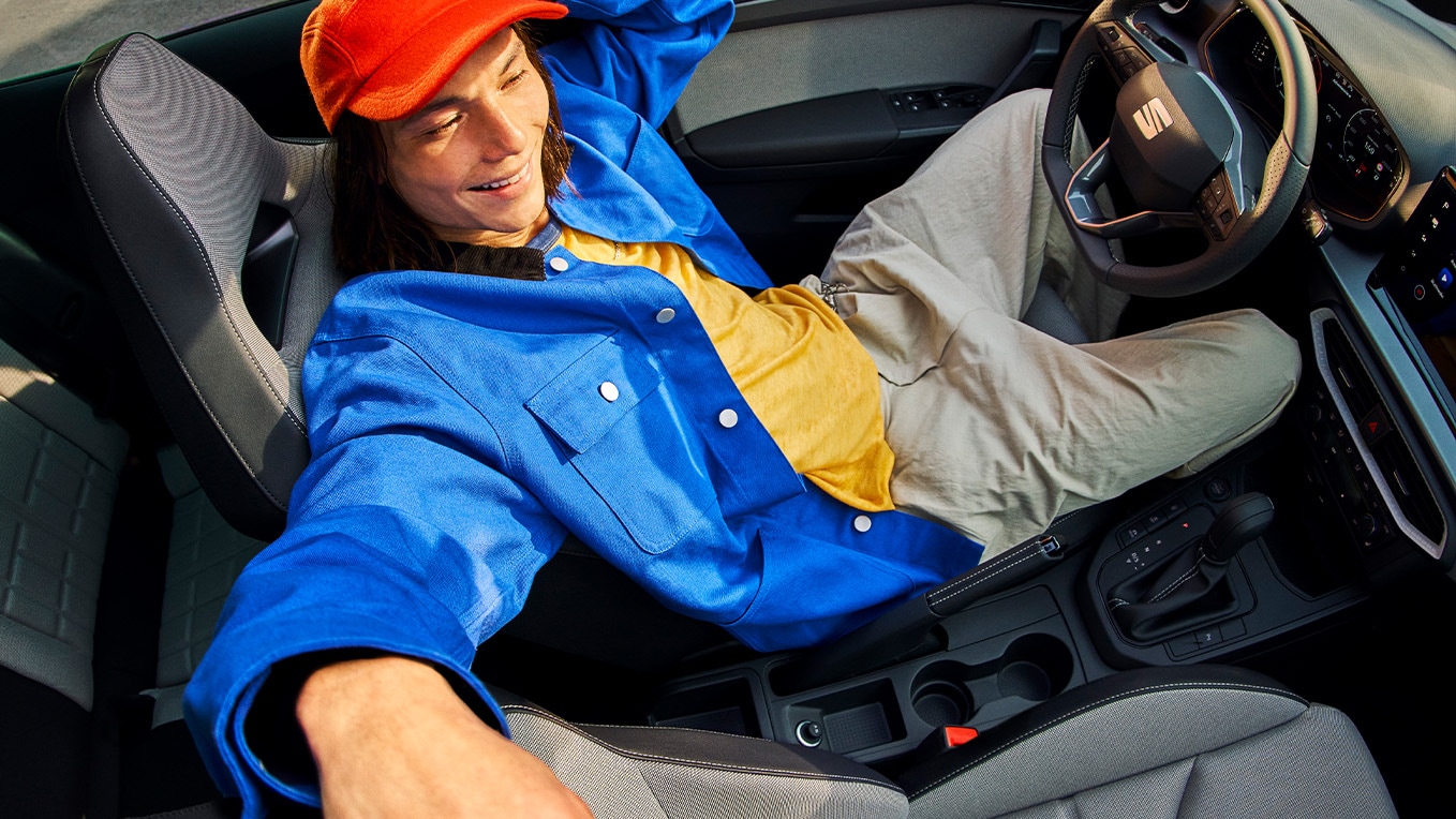 Interior del SEAT Ibiza, en el que se aprecia un salpicadero moderno, unos asientos elegantes y un techo solar abierto, con una persona recostada en el interior del coche.