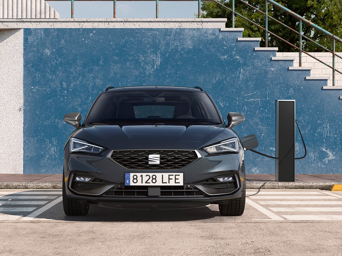 El SEAT León Sportstourer e-Hybrid, un coche eléctrico híbrido, estacionado en una plaza de aparcamiento junto a una estación de carga exterior, mostrando la función e-manager que aporta un increíble valor.