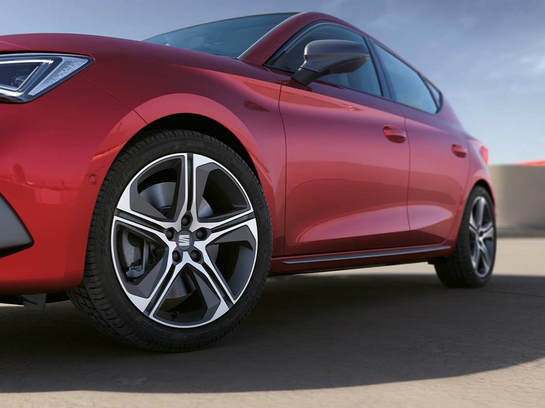 SEAT León Sportstourer en rojo Desire donde aparece la moldura lateral de la puerta y la llanta de aleación, con el coche aparcado bajo un cielo despejado.
