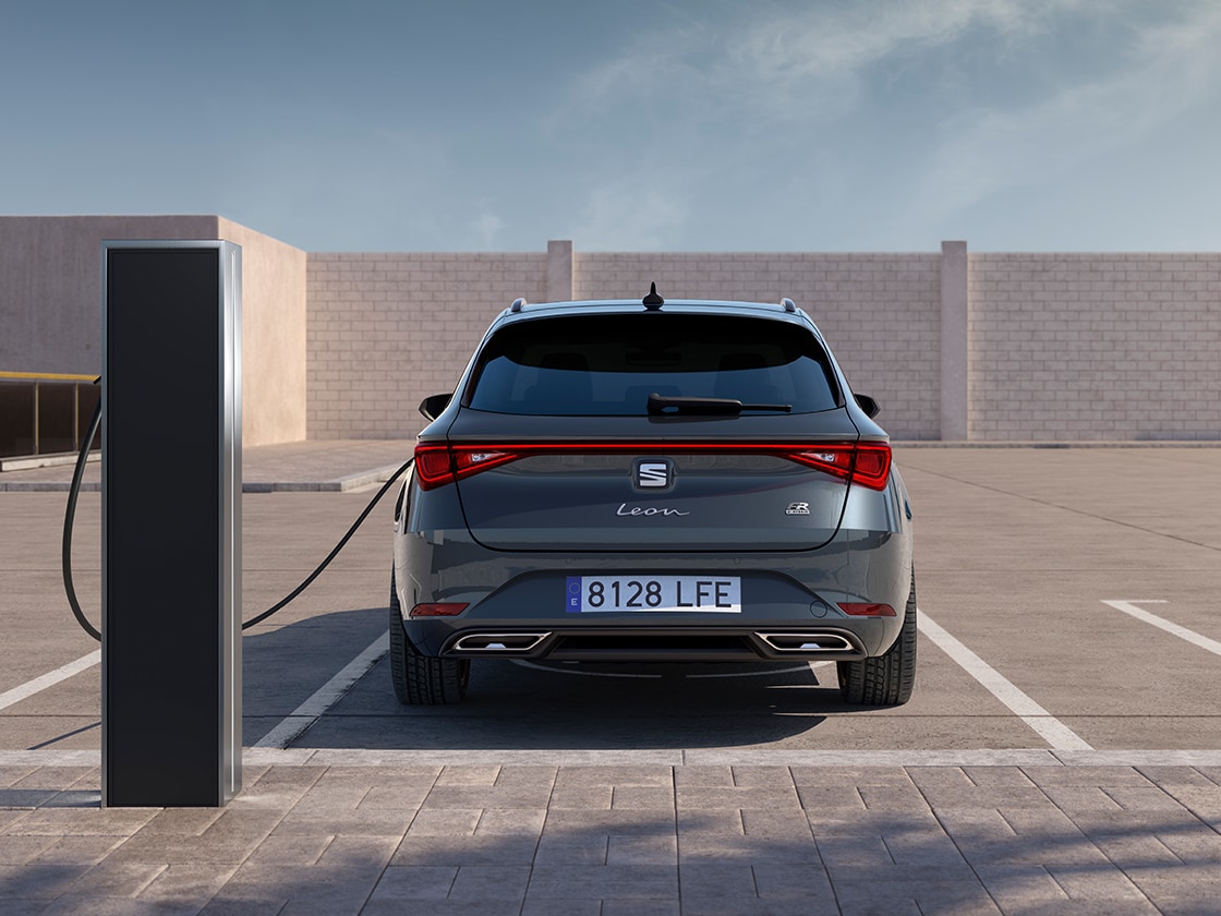 Vista trasera del SEAT León Sportstourer FR, carga automática del coche en una estación, nuevo compacto para 2025 en gris Magnetic, con sensores de aparcamiento delanteros y traseros y faros Matrix LED.
