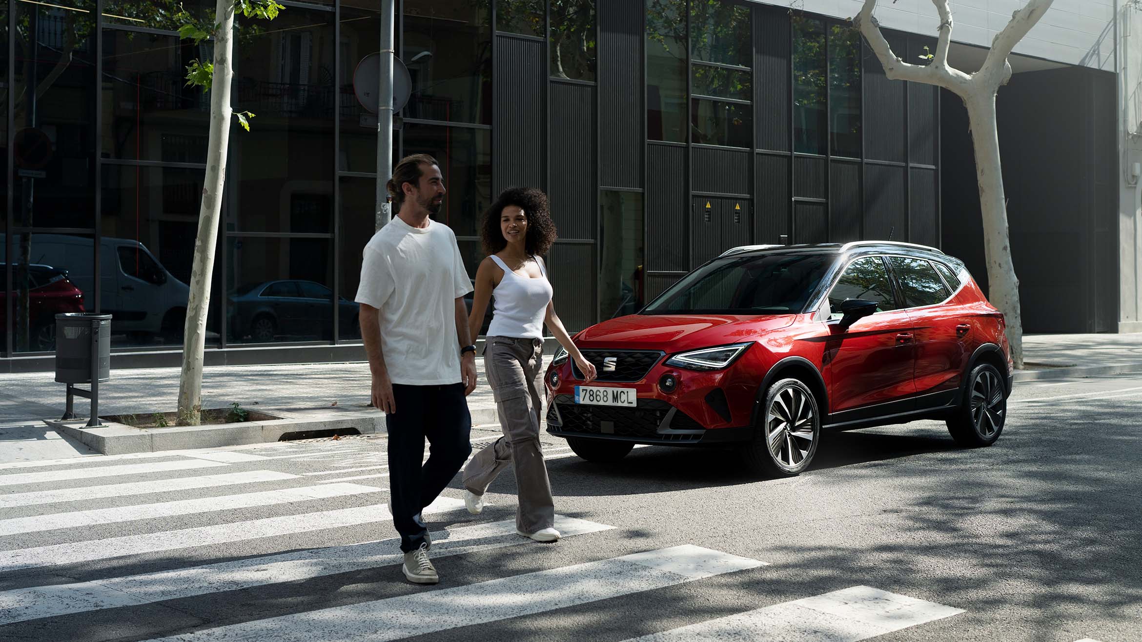 Hombre y mujer caminando frente a un SEAT Arona rojo bicolor