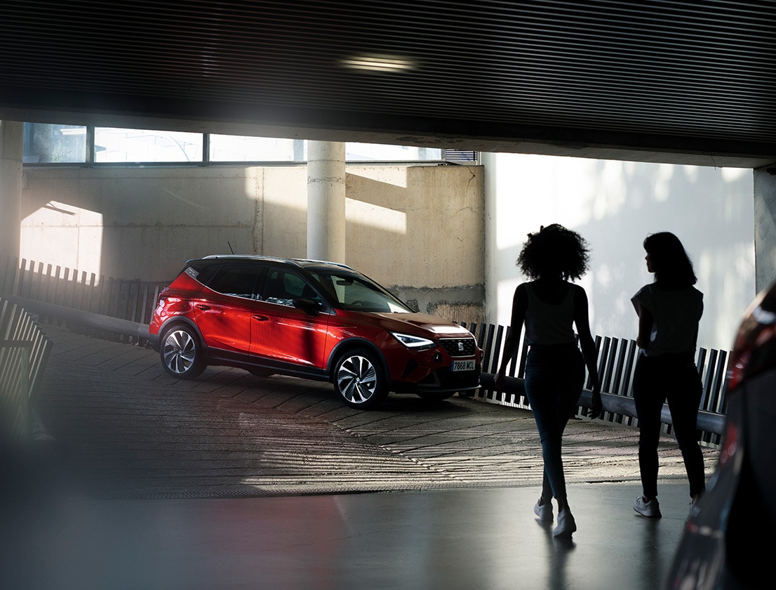 Mujeres en interior de un garage saliendo en dirección a un SEAT Arona rojo desire