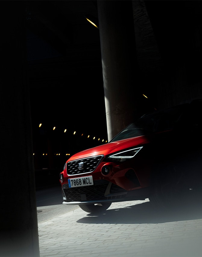 SEAT Arona SUV crossover en aparcamiento de noche con foco de luz iluminando parte delantera