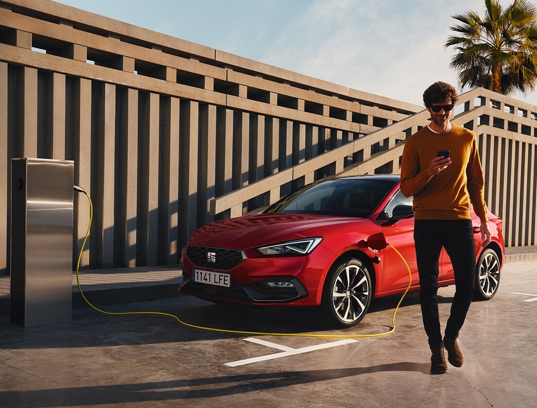 hombre alejándose del SEAT León e-HYBRID color rojo Desire usando su smartphone