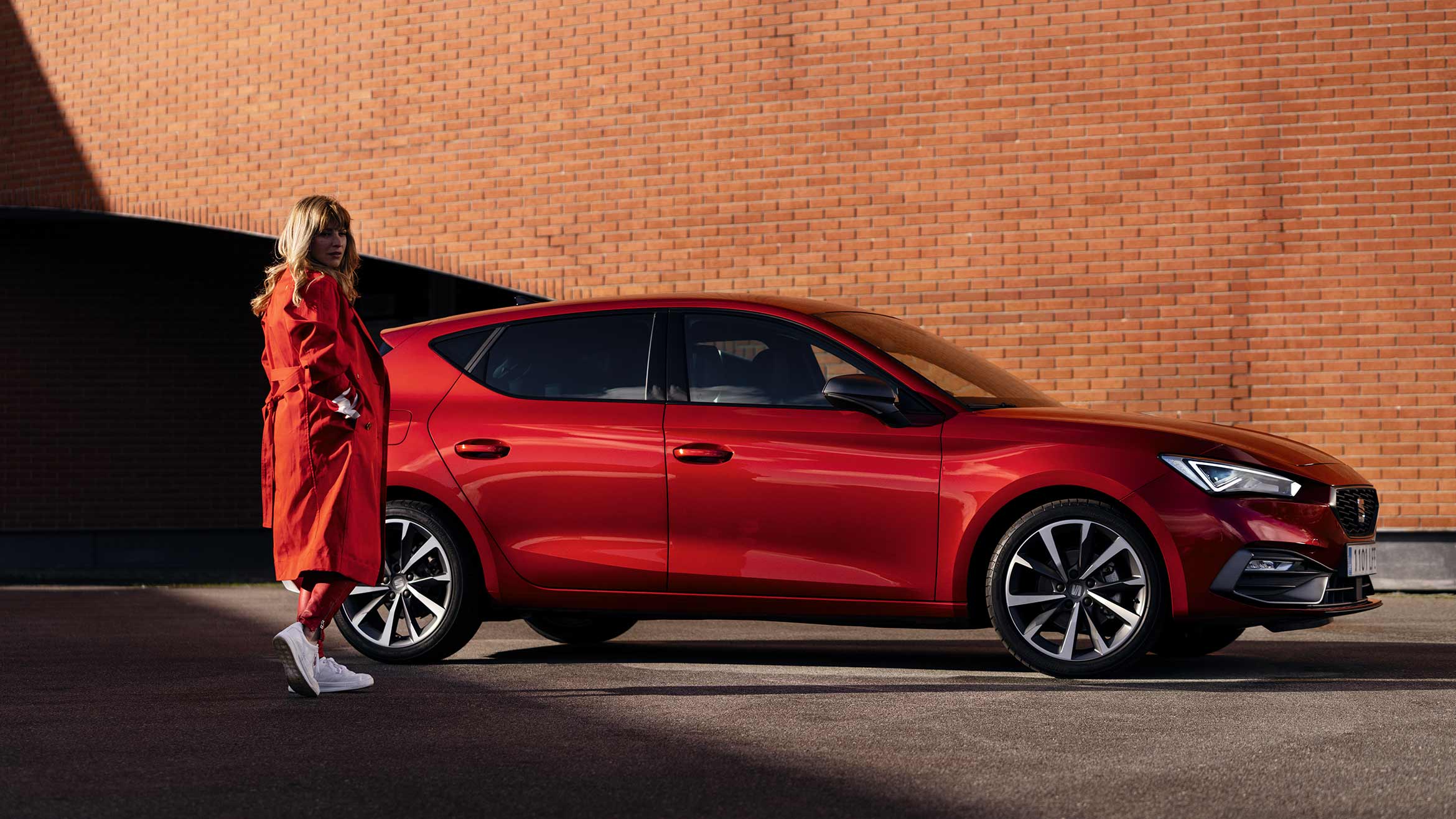 mujer con abrigo rojo de pie junto a seat León color rojo Desire