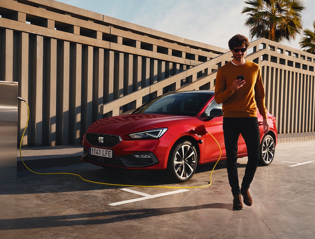 hombre alejándose del SEAT León e-HYBRID color rojo Desire usando su smartphone