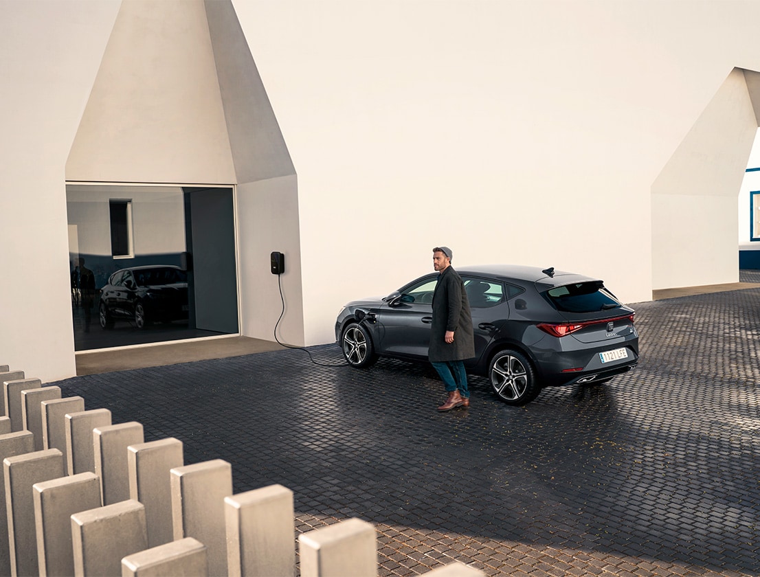 hombre alejándose del SEAT León e-HYBRID color rojo Desire usando su smartphone