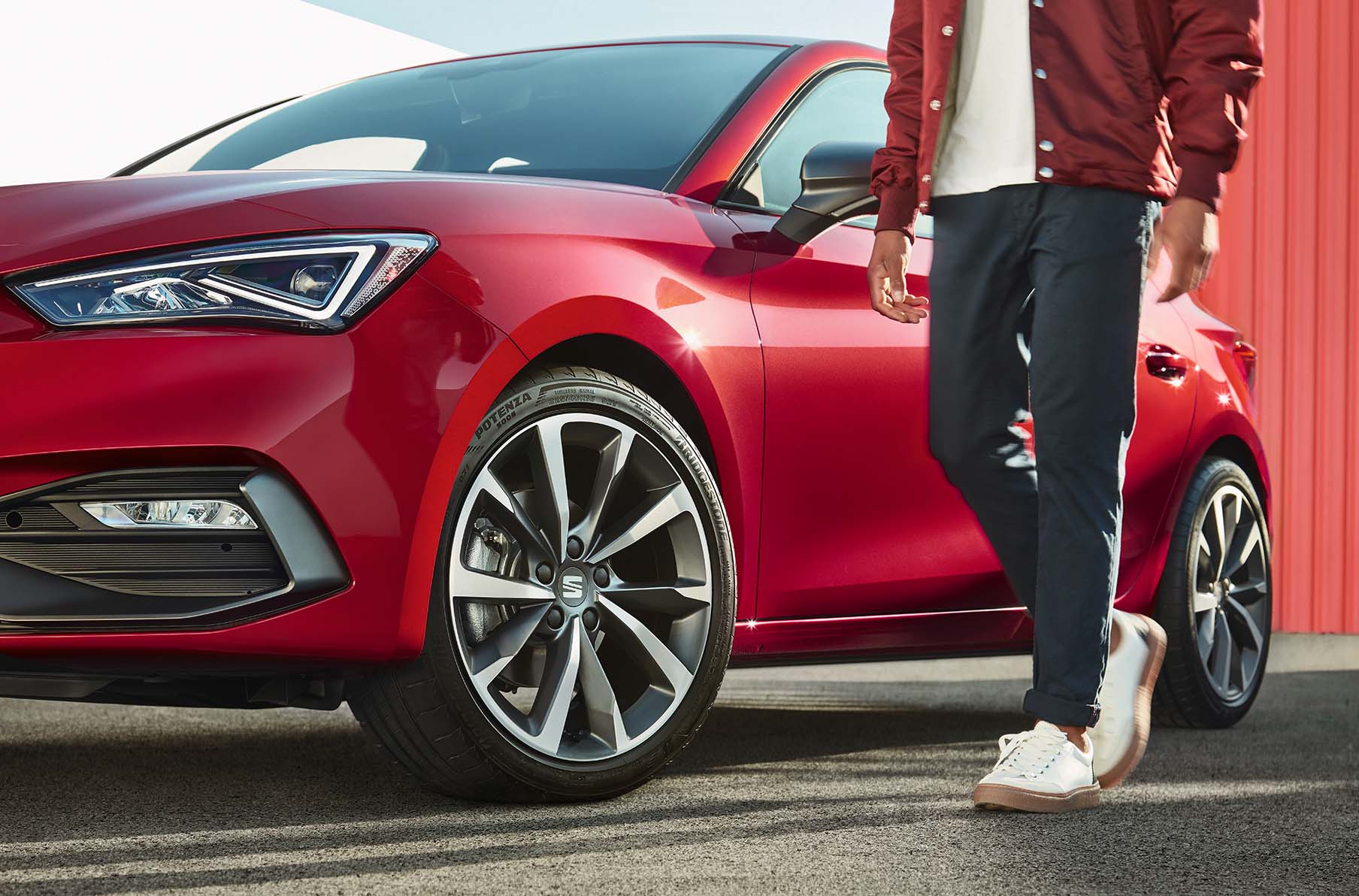 hombre de pie junto a SEAT León color rojo Desire con llantas de aleación gris Cosmo