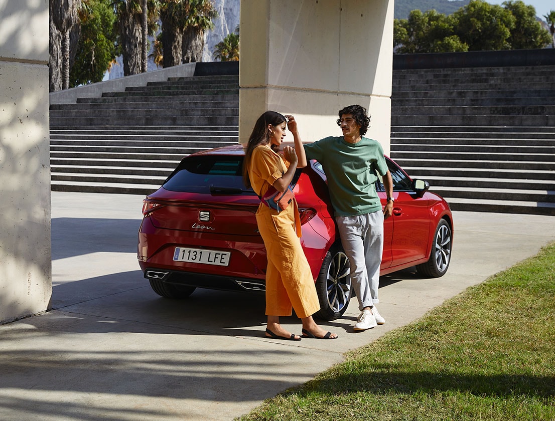 Pareja recostada en el nuevo SEAT León color rojo Desire