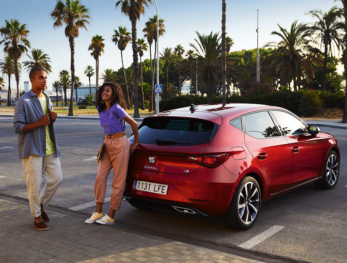 pareja hablando junto a un SEAT León color rojo Desire aparcado