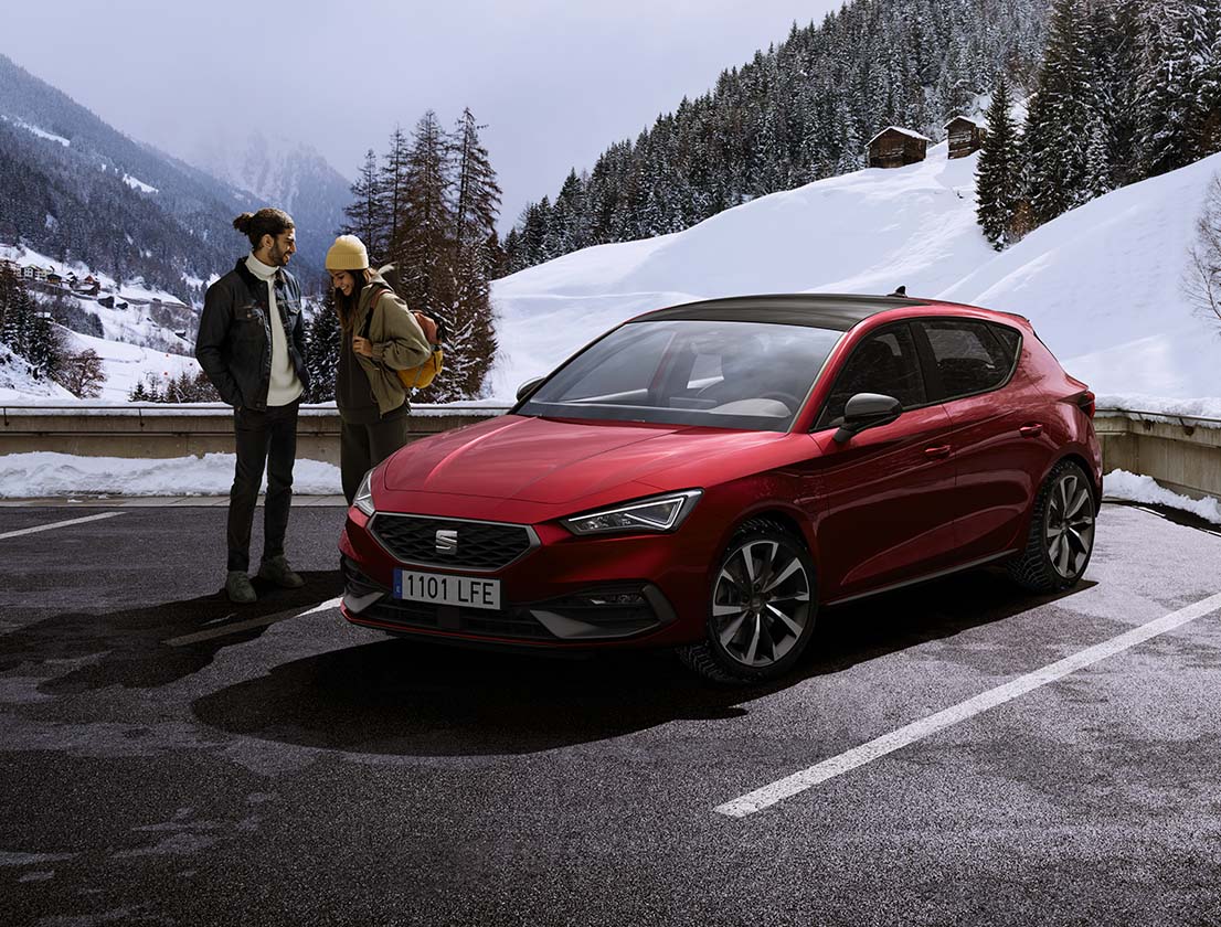 pareja conversando junto a un SEAT León color rojo Desire en una montaña nevada
