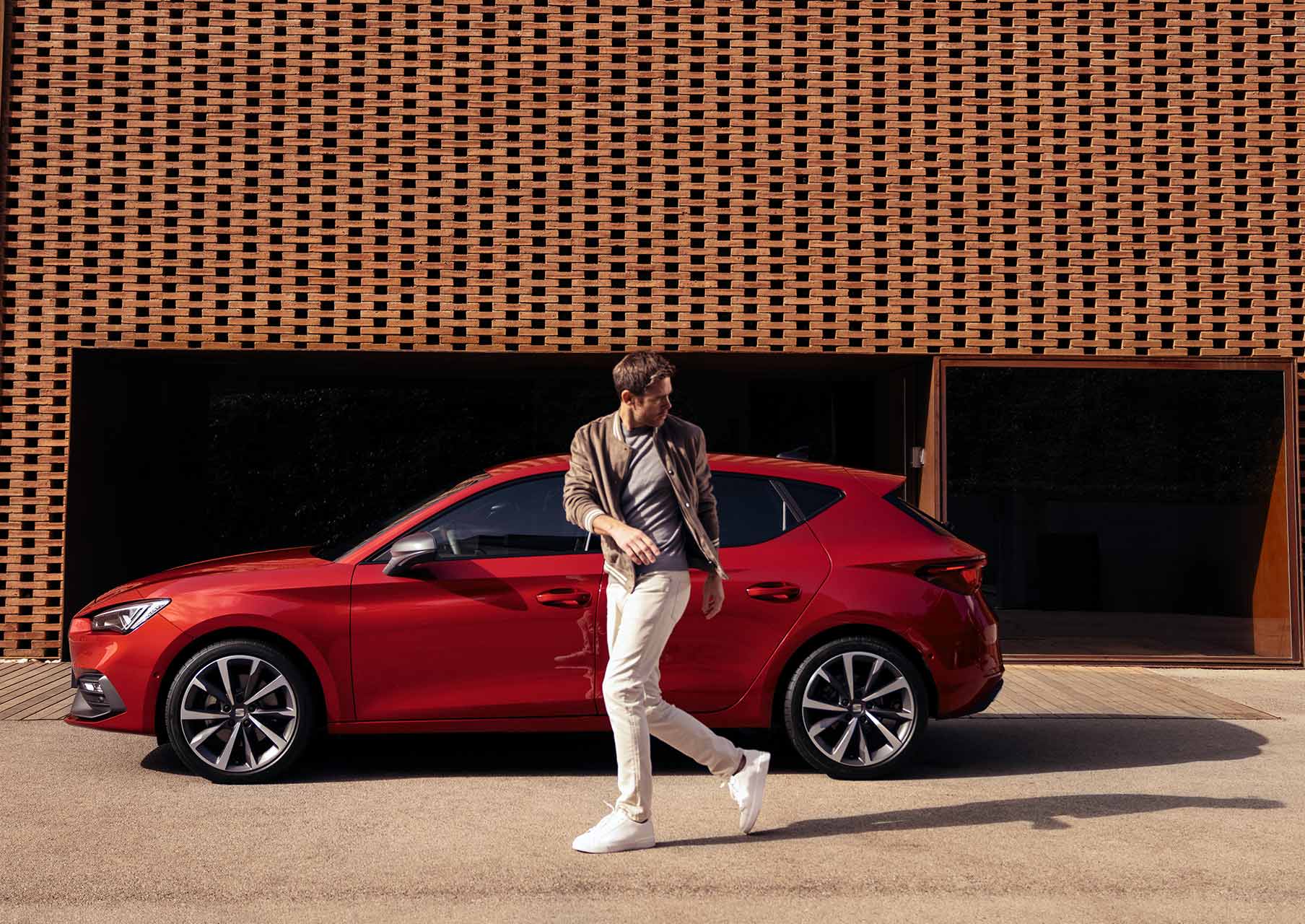 hombre caminando junto a SEAT León color rojo Desire con llantas de aleación