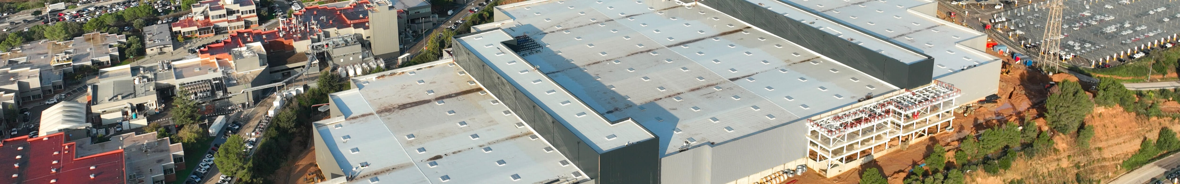 Vista aérea que mostrando un extenso complejo de fábricas con varios edificios grandes, amplias cubiertas y vías, bajo el cielo parcialmente nublado